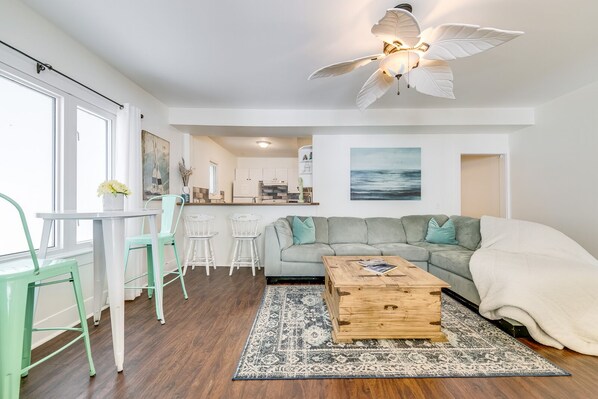 A modern living room with a grey sofa, a wooden coffee table, and a dining area with two chairs.