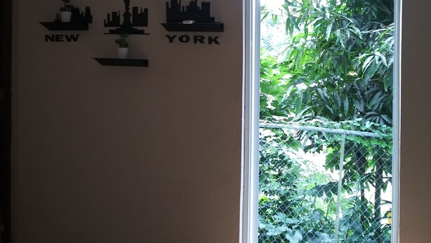 Una habitación con puerta corrediza de vidrio que da a un jardín, aire acondicionado instalado en la pared y un cuadro de arte mural con la ciudad de Nueva York.