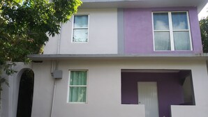 Un edificio de dos pisos con fachada morada y blanca, un pequeño porche y una puerta visible.