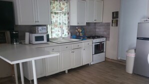 Una cocina con armarios blancos, microondas, estufa y refrigerador.