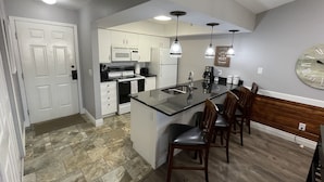 Una cocina moderna con una isla central, armarios blancos y un comedor con sillas de madera.