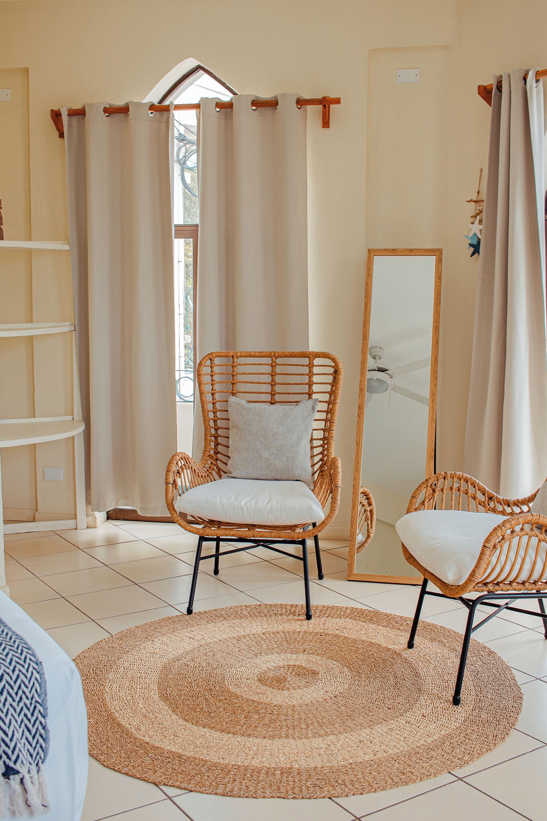 Una habitación con una silla de mimbre, un tapete redondo tejido y un espejo grande.