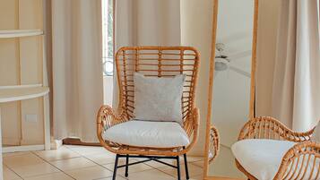 Una habitación con una silla de mimbre, un tapete redondo tejido y un espejo grande.
