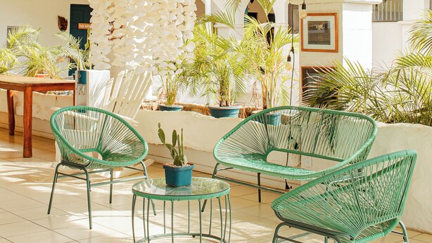 A spacious outdoor area with green wicker chairs, a table, and potted plants. - Zulu Surf Hotel (Tamarindo)