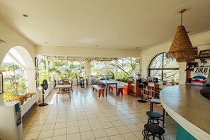 A spacious indoor area with multiple seating arrangements, including tables and benches, and a counter with stools. - Zulu Surf Hotel (Tamarindo)