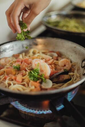 A hand adding parsley to a pan of seafood pasta on a stove. - Zulu Surf Hotel (Tamarindo)