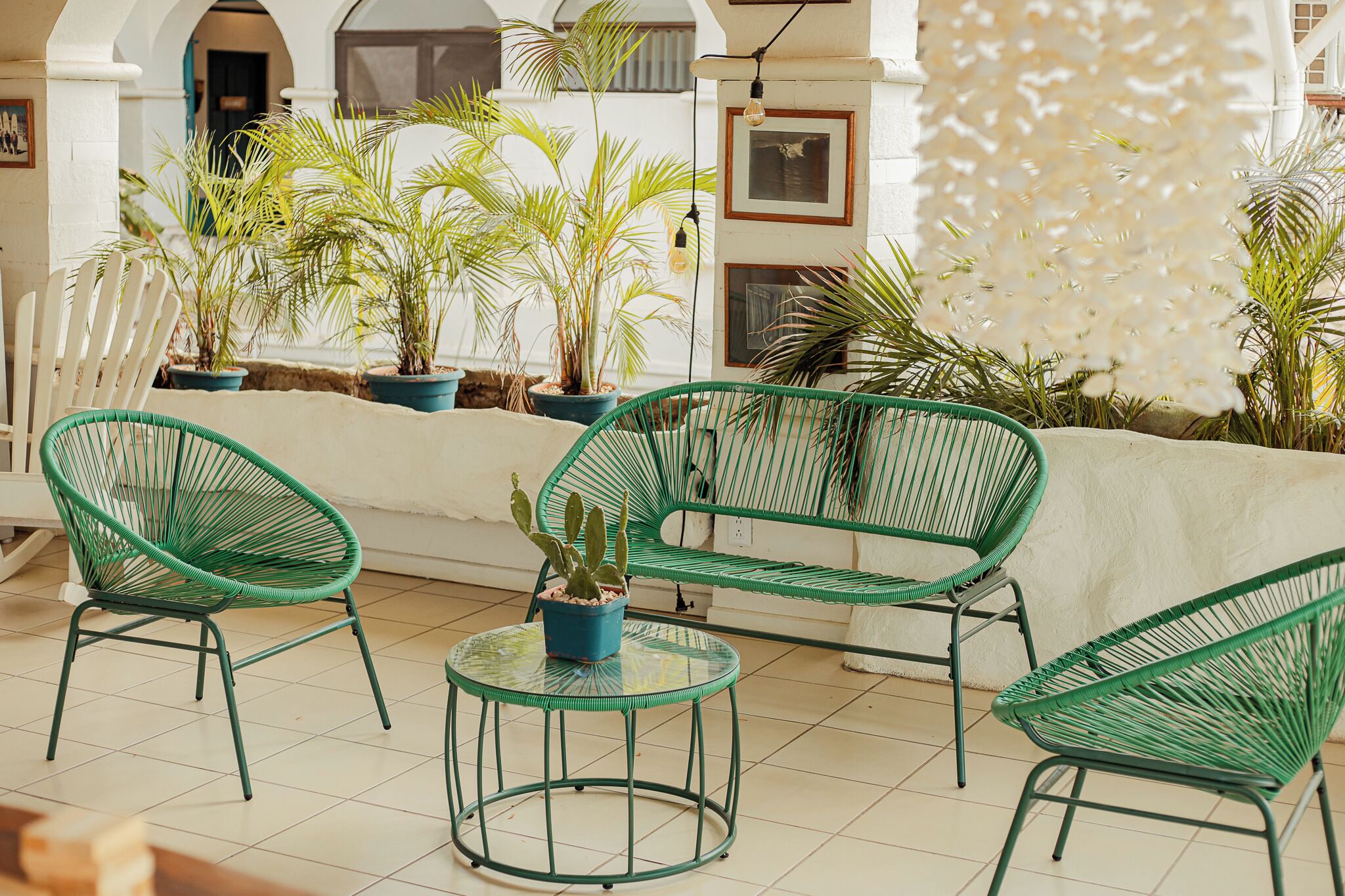 Un espace patio avec des fauteuils en osier vert, une petite table en verre et des plantes en pot.