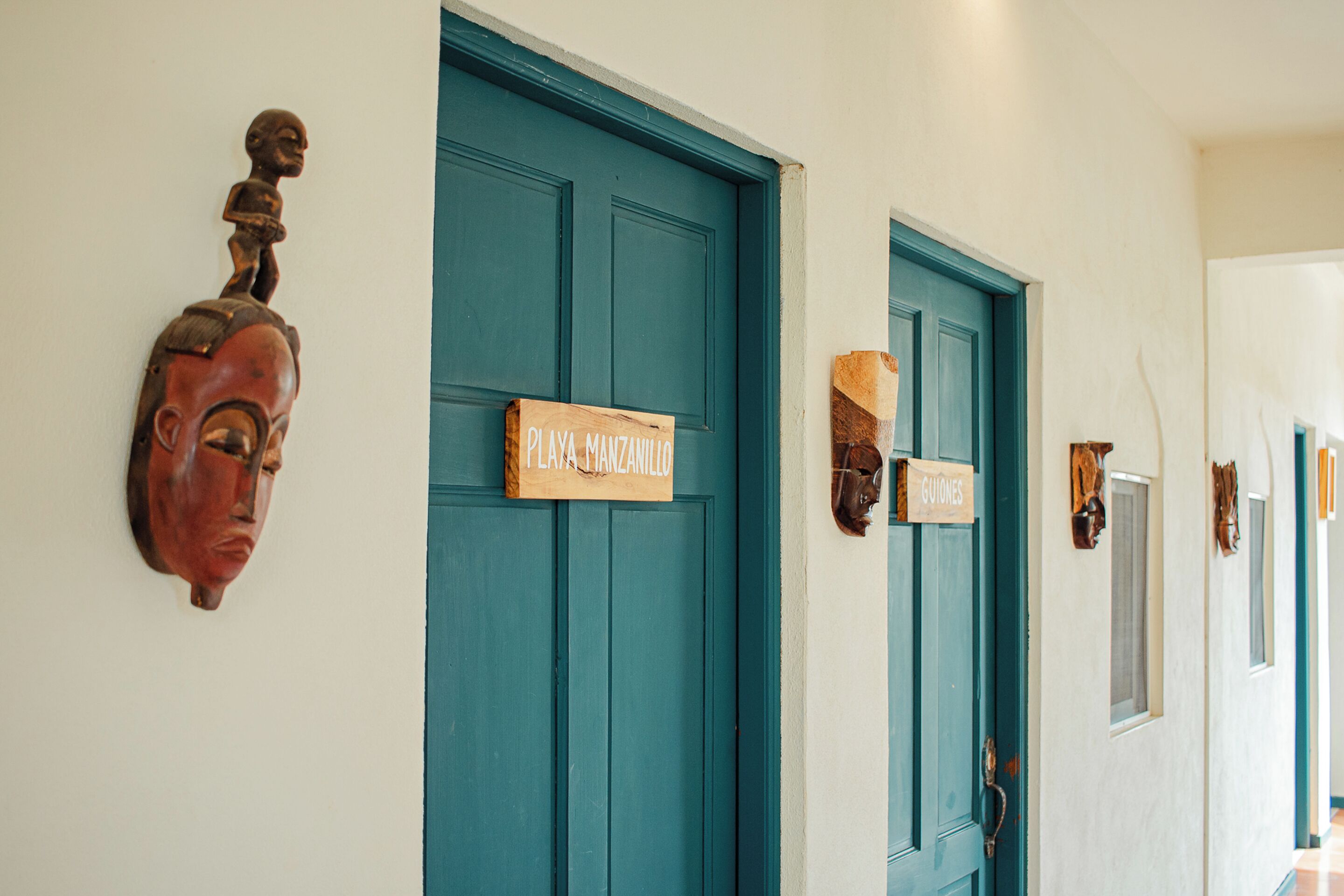 A hallway with teal doors, each with a wooden plaque.