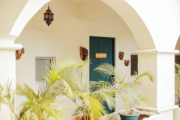 A white building with a teal door labeled "Playa Narano," surrounded by potted plants and an arched structure. - Zulu Surf Hotel (Tamarindo)