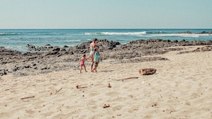 A sandy beach with rocky outcrops and a clear sky. - Zulu Surf Hotel (Tamarindo)