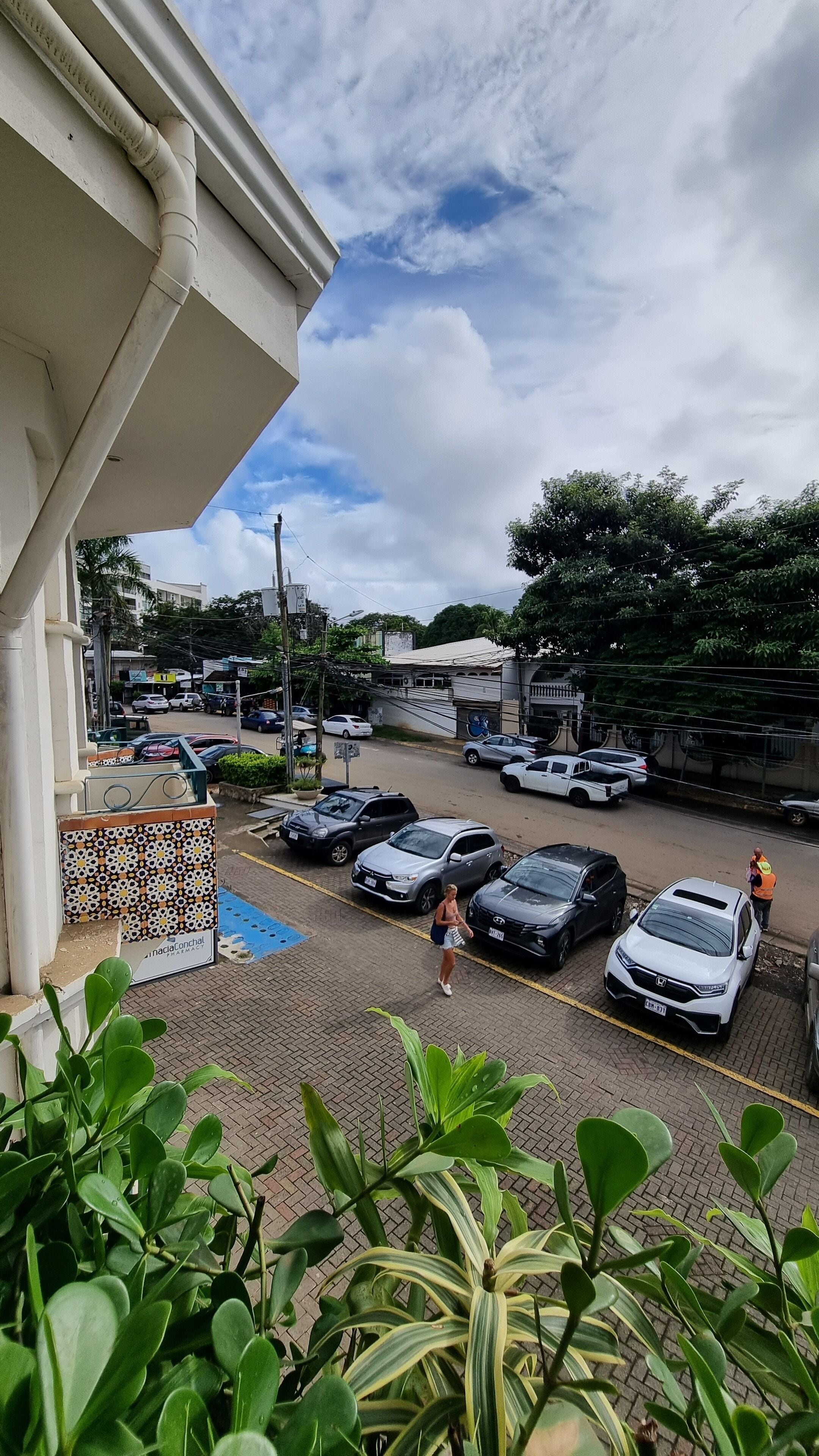 A parking area with several cars, a pharmacy, and a person walking.