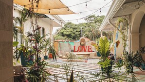 A courtyard with potted plants, a tiled floor, and a 'LOVE' sign. - Zulu Surf Hotel (Tamarindo)
