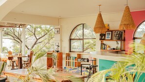 A cozy, well-lit room with a large window, wooden furniture, and hanging woven light fixtures. - Zulu Surf Hotel (Tamarindo)