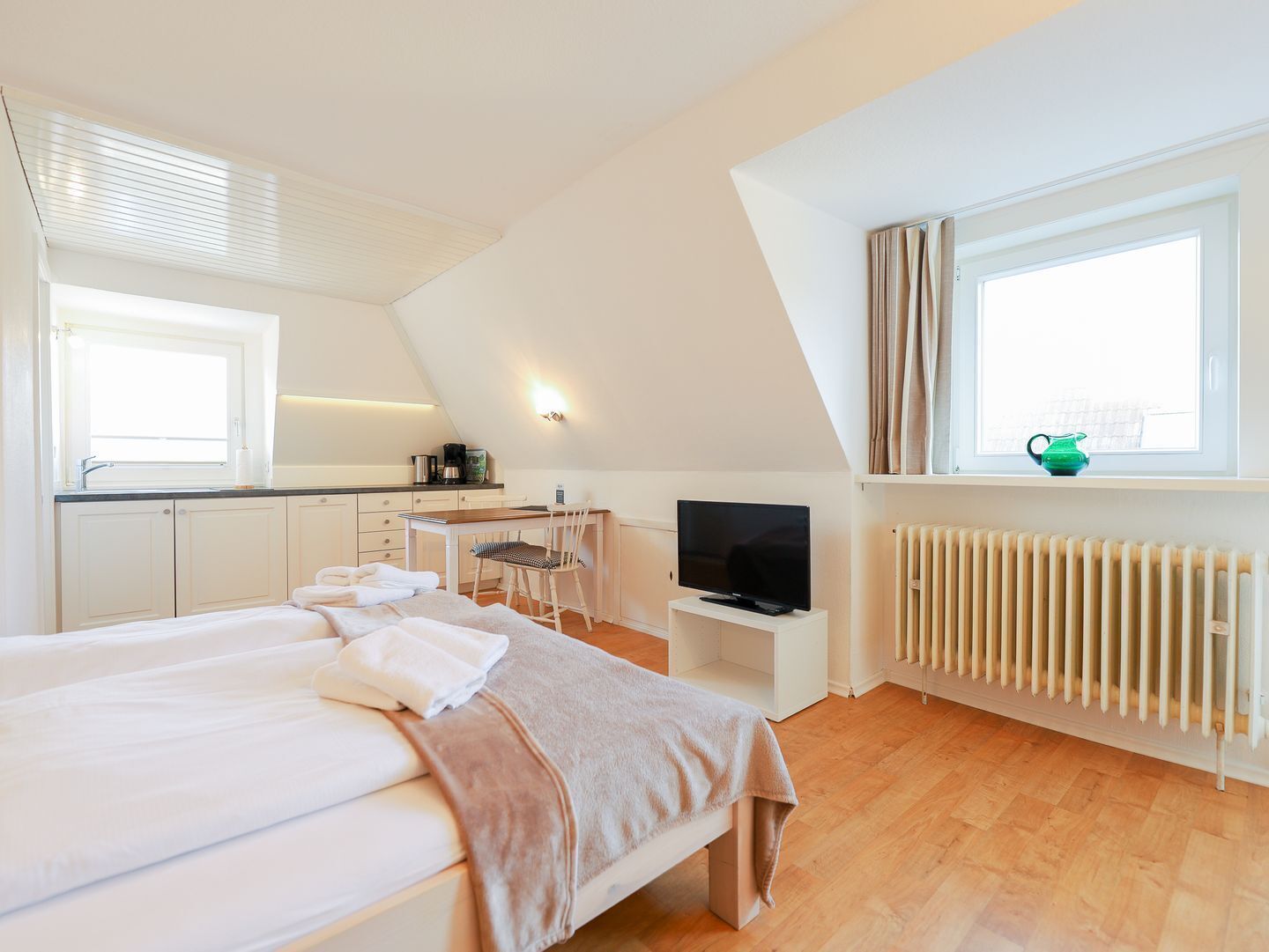 A bedroom with a bed, a desk, a TV, and a window.