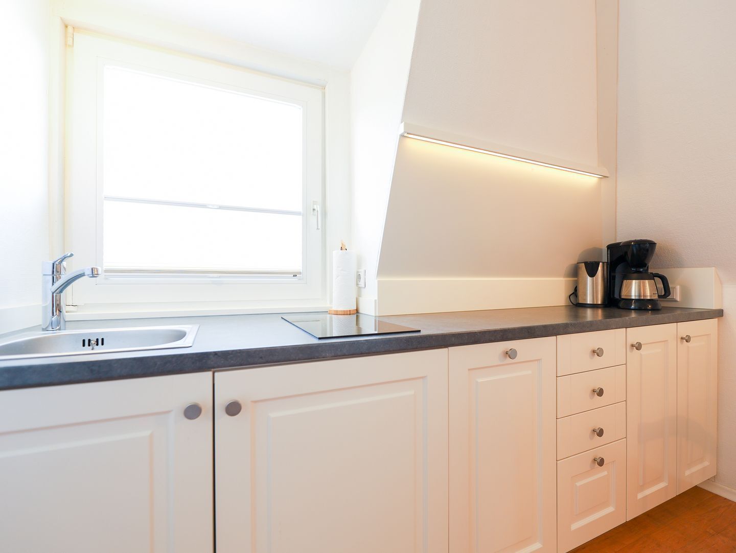 A modern kitchen with white cabinets, a stainless steel sink, a window, and a coffee maker.