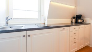 Una cocina moderna con armarios blancos, un lavamanos de acero inoxidable, una ventana y una cafetera.