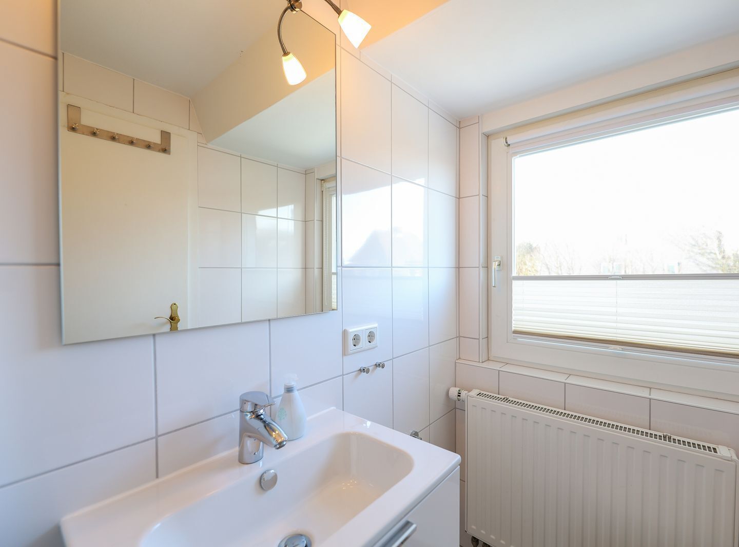 Un baño con lavamanos blanco, espejo y ventana.