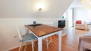 Una cocina moderna con una mesa de madera y sillas blancas, un televisor y un pequeño comedor.