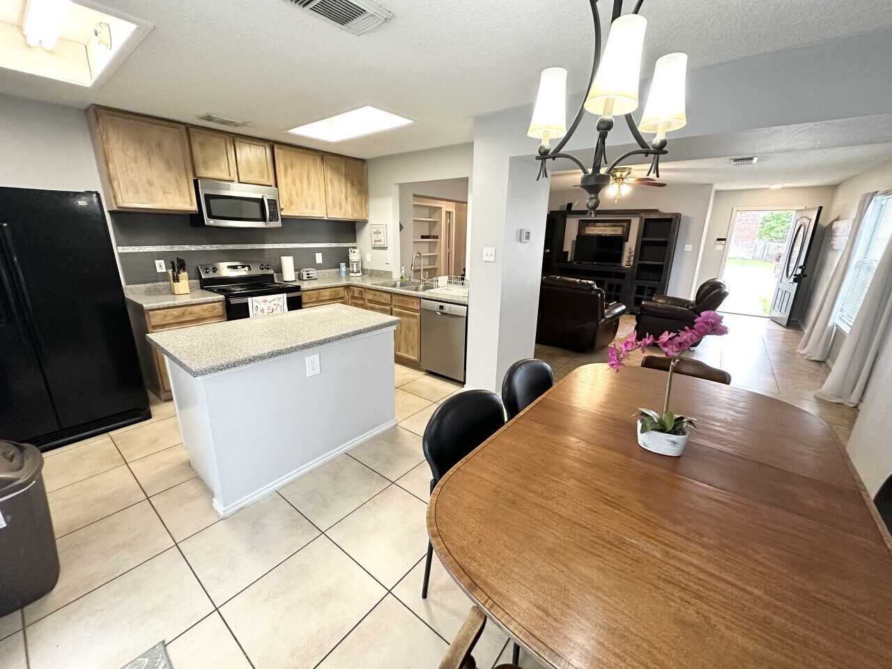 Una cocina moderna con una isla central, un comedor con mesa de madera y vista al salón.