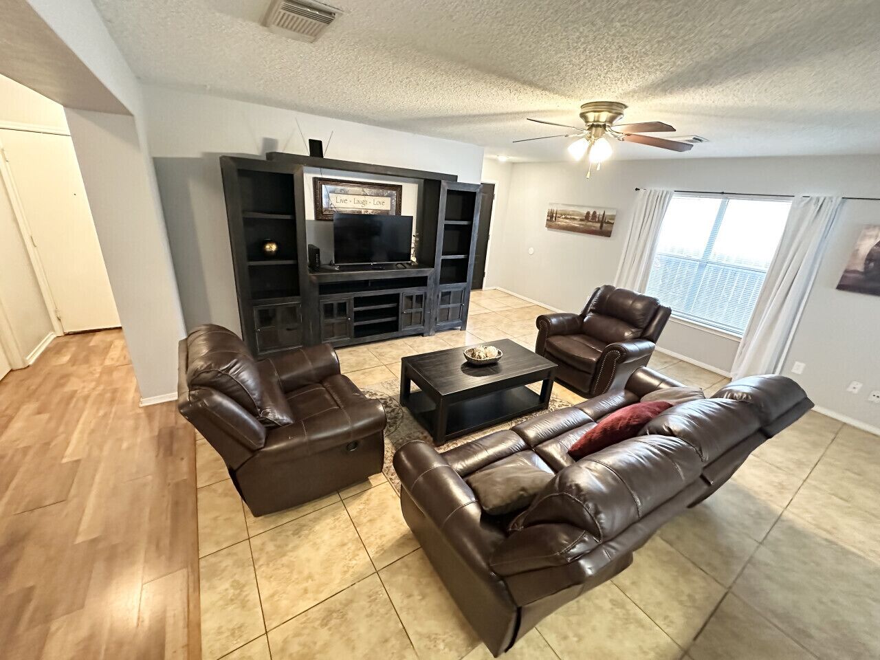A living room with a TV, leather sofas, a coffee table, and a ceiling fan.