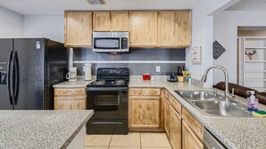 Una cocina con armarios de madera, un refrigerador de acero inoxidable, un microondas, una estufa y un lavaplatos.