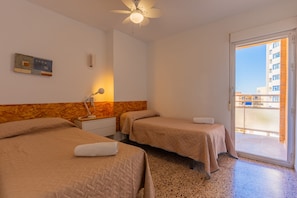 A hotel room with two beds, a ceiling fan, a nightstand with a lamp, a small table, and a sliding glass door to the outside. - 4D MAR2 Apartment, 2 bedrooms (Calpe/Calp)