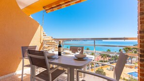 A balcony with a table set for two, overlooking a coastal view.
