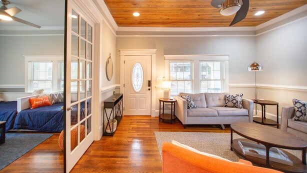 A spacious living room with hardwood flooring, a sofa set, a coffee table, and a door leading to another room.