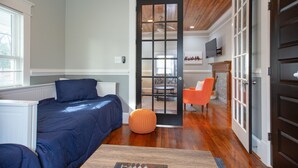 A bedroom with a bed, a small orange ottoman, and a wooden floor.