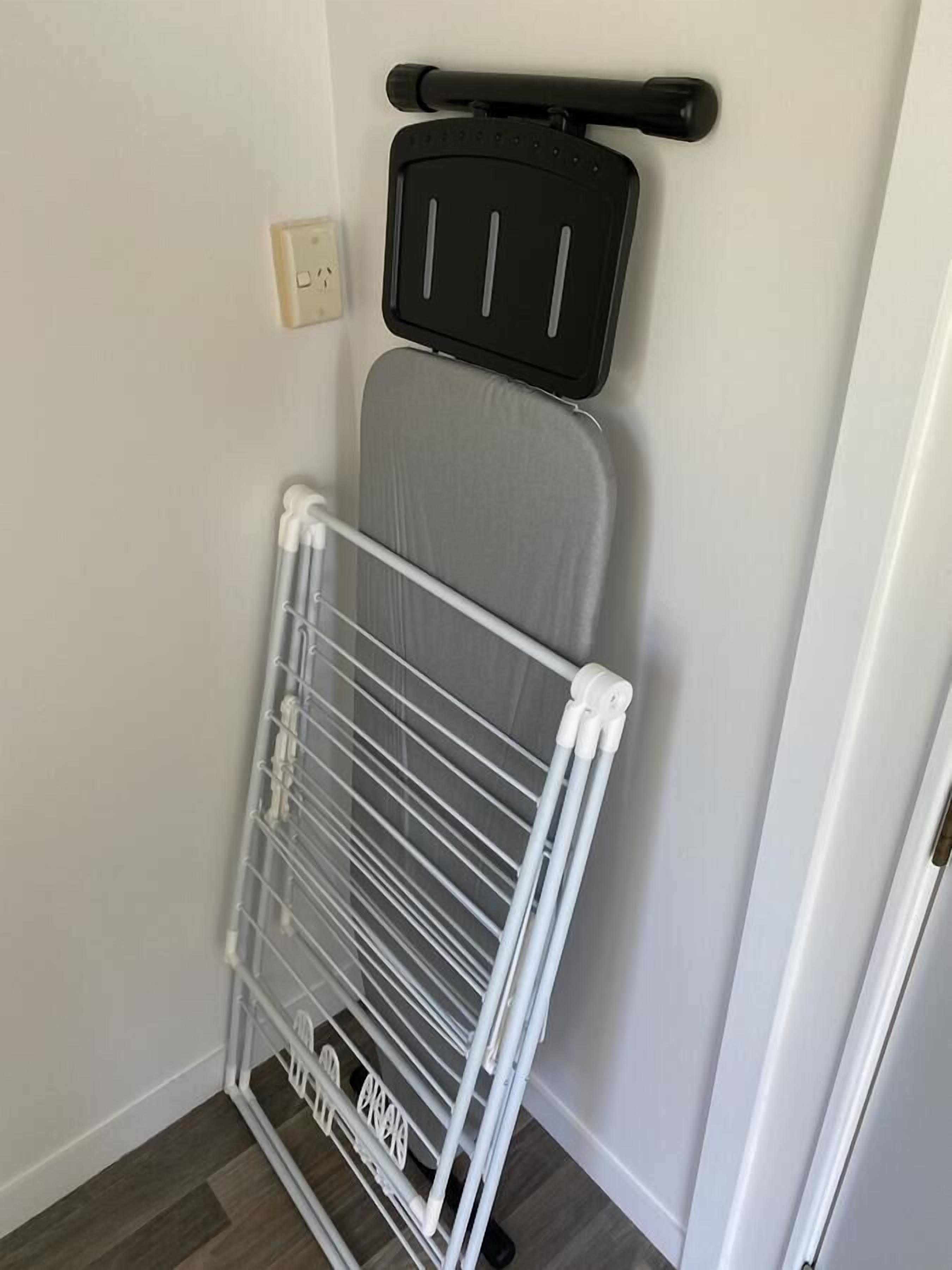 Une petite pièce avec un radiateur blanc, une planche à repasser grise et un étendoir blanc.