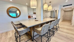 A modern kitchen with a central island, pendant lighting, wicker chairs, and a large mirror. - Gulfside Place #107 ~ 3br/3ba - Gulf front living at its finest (Sanibel)