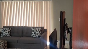 Ein Wohnzimmer mit grauem Sofa, gemusterten Kissen, einem Gemälde über dem Sofa und einem Fernseher auf einem Schrank.