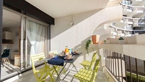 Un balcon avec des chaises jaunes, une table dressée avec des aliments pour le petit-déjeuner et une vue sur un immeuble moderne doté de balcons.