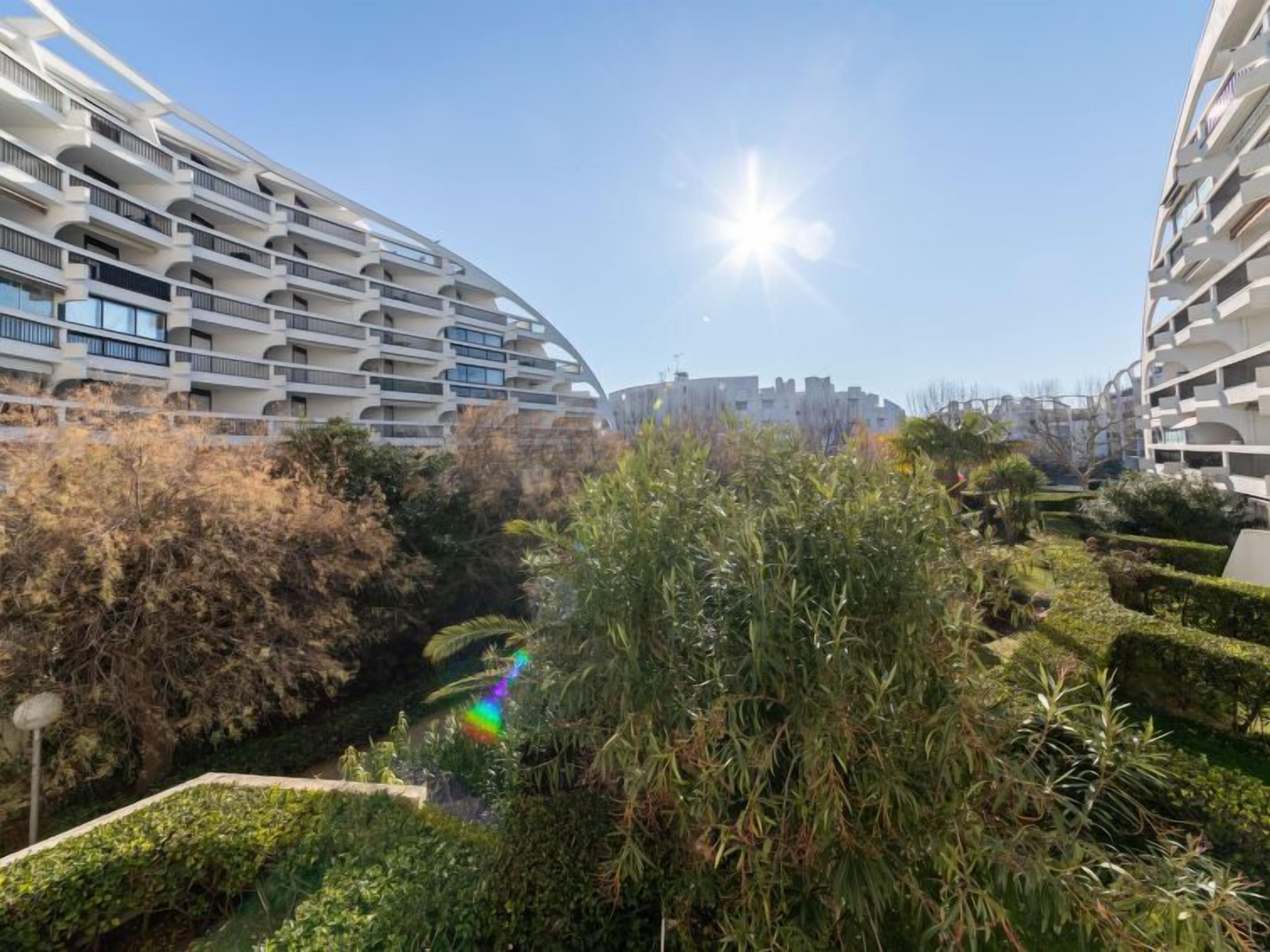 Un complexe résidentiel moderne doté de nombreux balcons, d’un jardin central et offrant une vue sur un ciel dégagé.