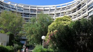 Un bâtiment moderne à plusieurs étages, doté d’une façade incurvée, entouré d’une végétation luxuriante et surplombé d’un ciel bleu clair.