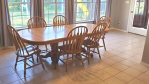 Un espace repas comprenant une table et des chaises en bois, de grandes fenêtres et une porte.