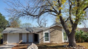 Une maison de plain-pied avec un garage, une cour avant avec un arbre et une boîte aux lettres.