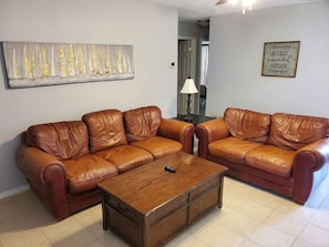 Een woonkamer met twee bruine leren banken, een houten salontafel, een lamp en een kunstwerk aan de wand.