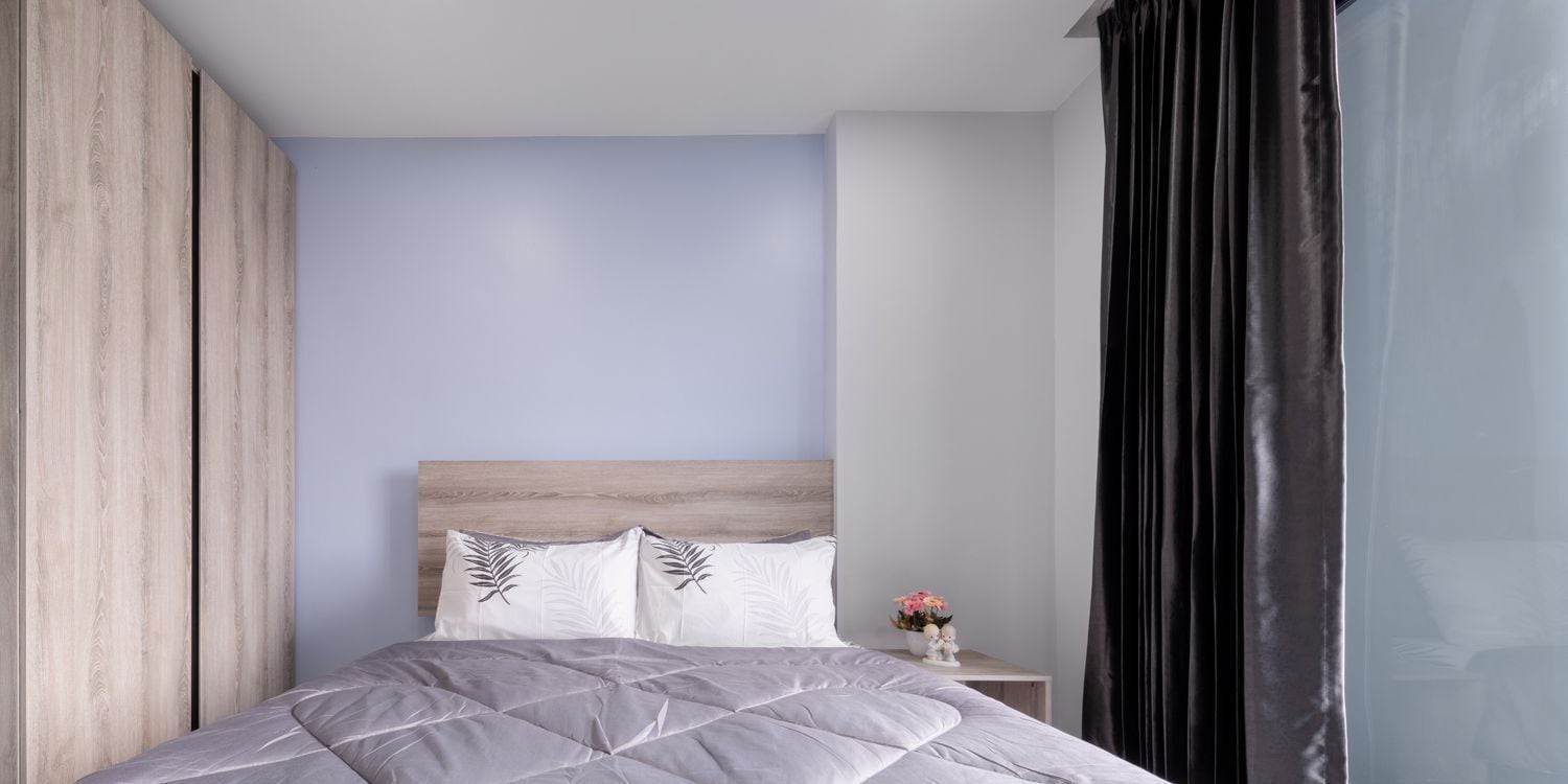 A modern bedroom with a wooden headboard, a grey quilted bedspread, and a small bedside table with a vase of flowers.