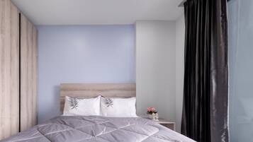 A modern bedroom with a wooden headboard, a grey quilted bedspread, and a small bedside table with a vase of flowers.