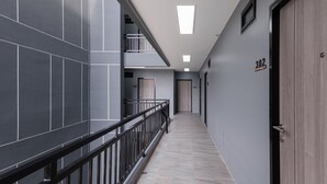 A modern hallway with grey tiled walls, a wooden door labeled "302", and a metal railing. - Aqua Residences (Bangkok)