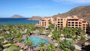 Ett semesterparadis med en stor pool omgiven av palmer, ett berg i bakgrunden och en fri utsikt över havet.