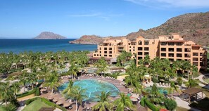 Ett semesterparadis med en stor pool omgiven av palmer, ett berg i bakgrunden och en fri utsikt över havet.