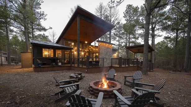 A lodge with a fire pit surrounded by Adirondack chairs, a stone fireplace, and a covered deck area. - Cabin Therapy - Luxury Cabin Near ATV Trails (Broken Bow)
