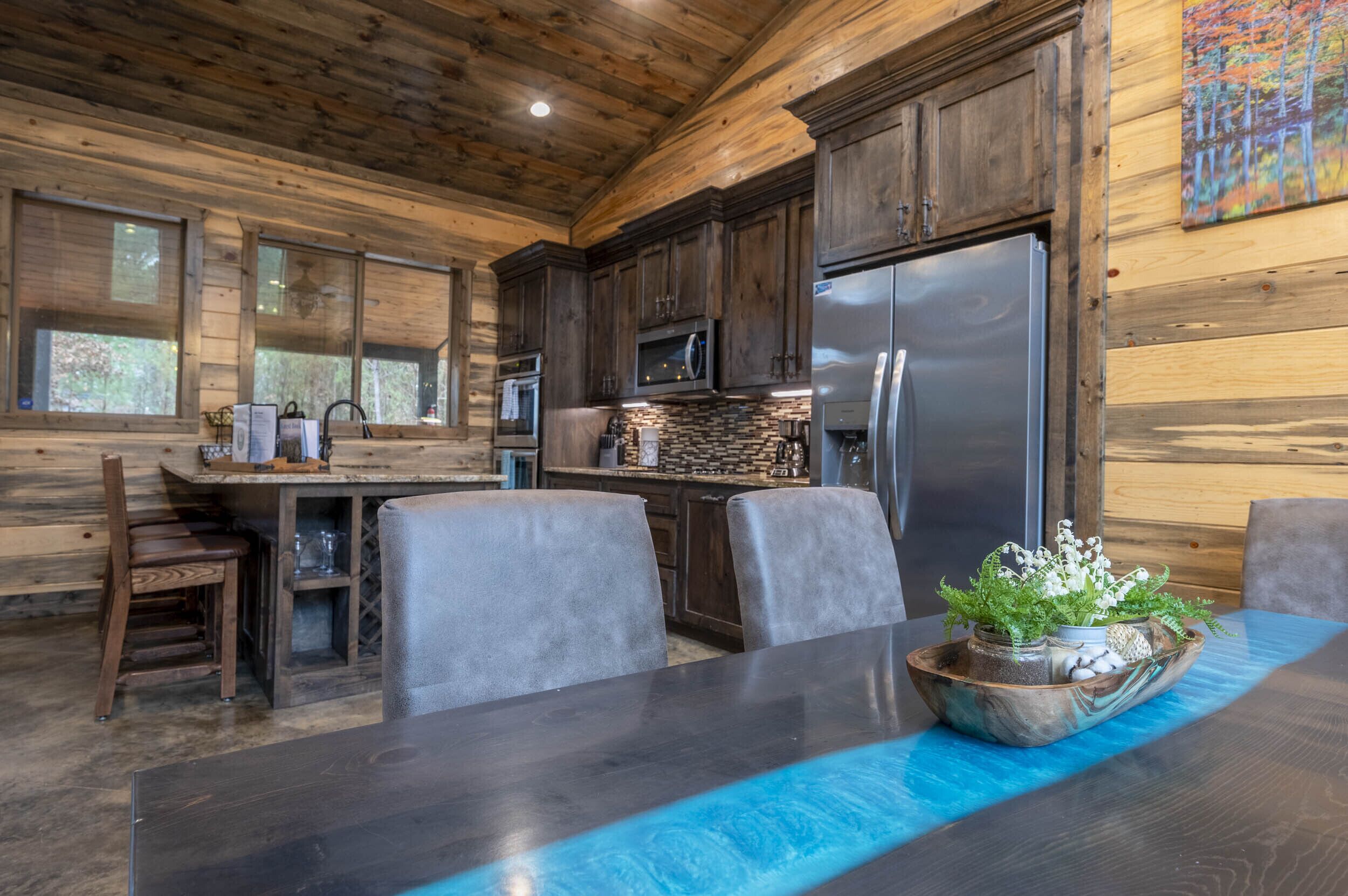 L’intérieur d’un chalet rustique comprend un coin repas, des murs en bois, une cuisine équipée d’appareils modernes et une grande fenêtre.