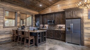 A rustic cabin-style kitchen with wooden walls, a stone backsplash, and a large refrigerator. - Cabin Therapy - Luxury Cabin Near ATV Trails (Broken Bow)