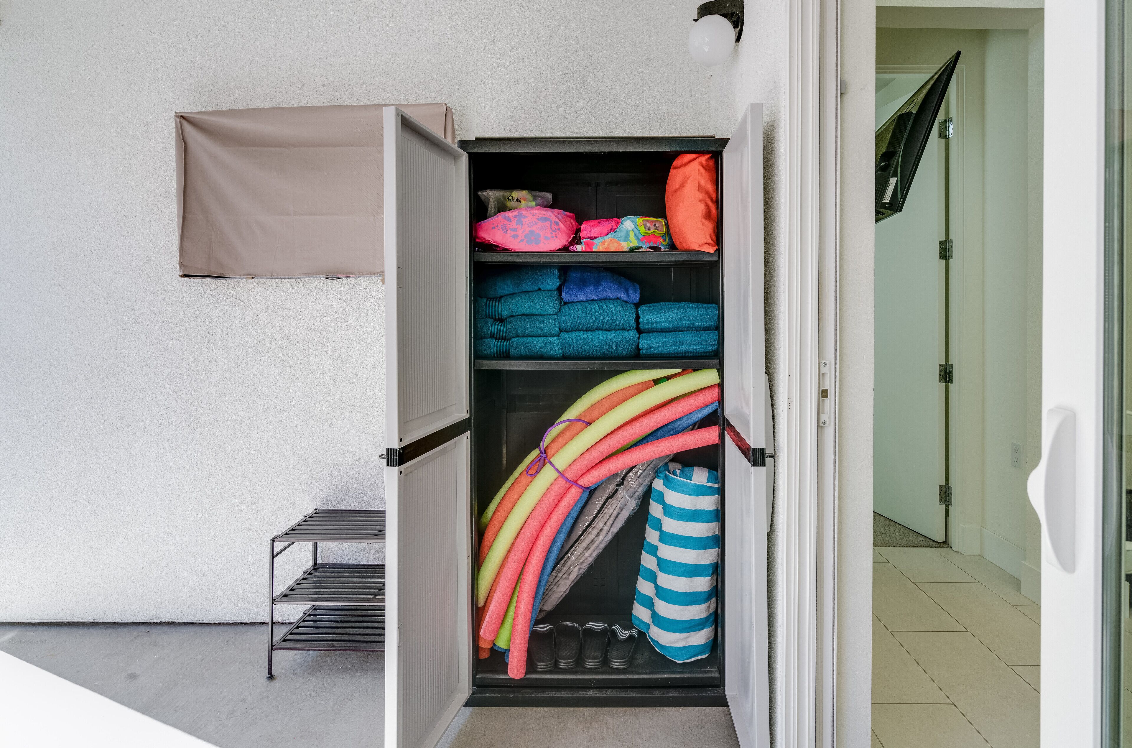 A storage unit with shelves containing folded towels, a striped bag, and a pair of shoes.