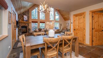 A spacious dining area with a wooden table and chairs, a stone fireplace, and large windows allowing natural light.