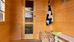 L’intérieur d’un chalet en bois, avec une porte, une serviette suspendue, un banc et un panier tressé rempli de bois de chauffage.