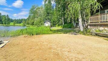 A sandy beach area with a small wooden structure, a wooden deck, and a lake in the background.